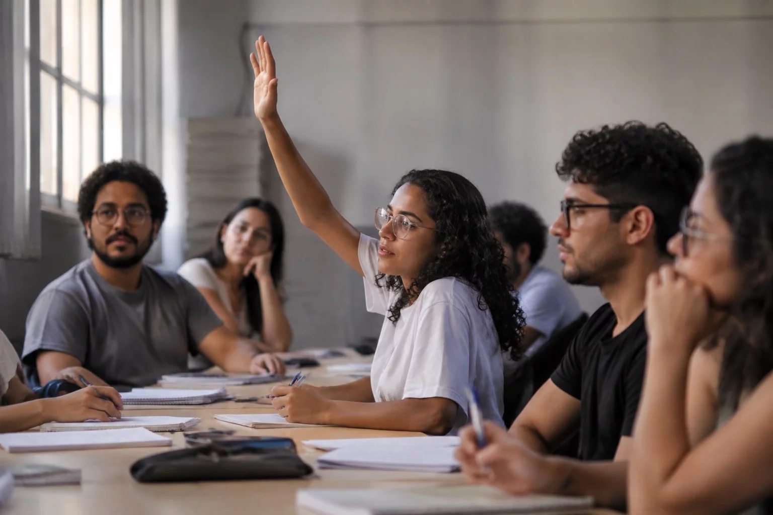 Estudante levantando a mão em uma mesa de seminário coberta de anotações